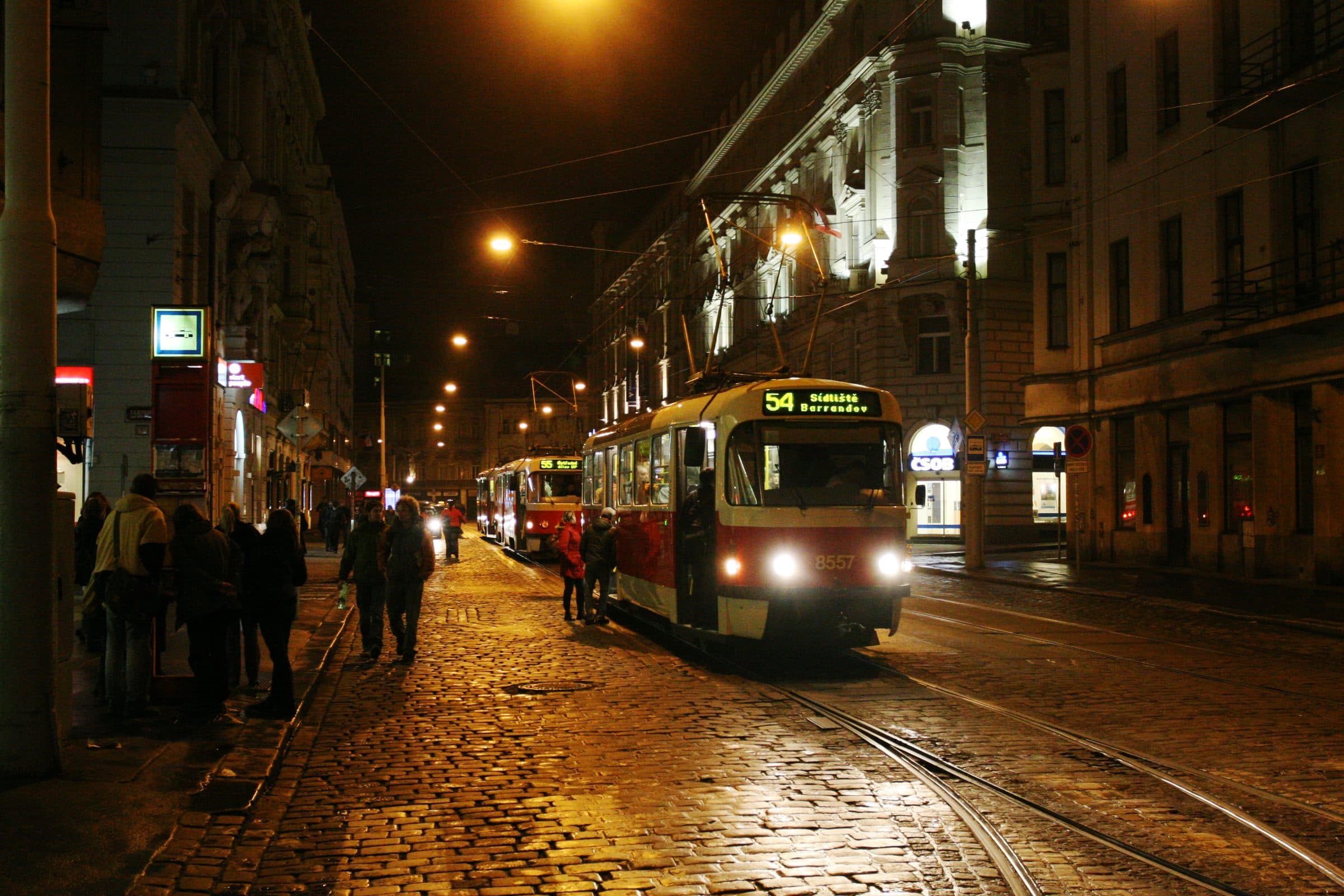 Noční pražská ulice s tramvají a lidmi na zastávce
